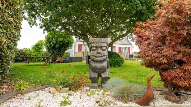 Un jardin avec une statue en pierre, une clôture en bois et une maison en arrière-plan.