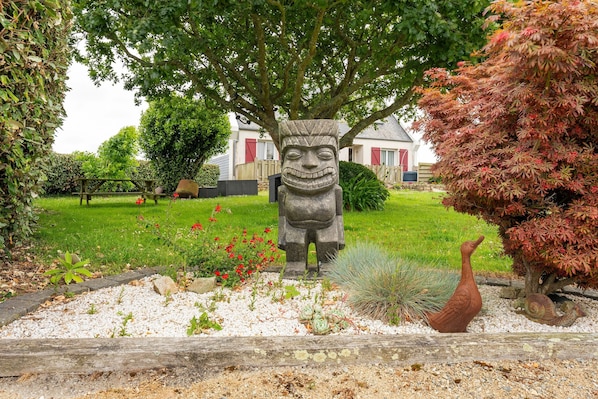 Un jardin avec une statue en pierre, une clôture en bois et une maison en arrière-plan.