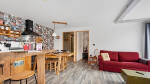 Une cuisine avec un plan de travail en bois, des tabourets et un canapé rouge dans l’espace salon.