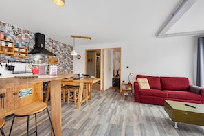 Une cuisine avec un plan de travail en bois, des tabourets et un canapé rouge dans l’espace salon.