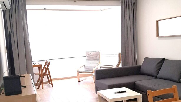 Una sala de estar moderna con un sofá, una mesa de centro, un escritorio con una computadora portátil y un balcón con una silla.
