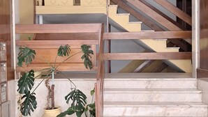 Una escalera con barandilla de madera y peldaños color beige, que conduce a un rellano con una planta en maceta.