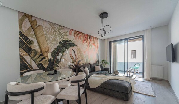 Ein modernes Wohnzimmer mit einem Glastisch, einer Couch und einem großflächigen Wandbild mit tropischen Motiven.