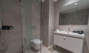 Ein modernes Badezimmer mit einer Duschkabine aus Glas, einer Toilette und einem weißen Waschtisch mit Spiegel.