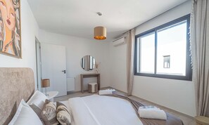 Ein Hotelzimmer mit Bett, Nachttisch, Lampe, Spiegel und einem großen Fenster.