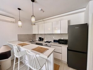 Eine moderne Küche mit weißen Schränken, einem schwarzen Kühlschrank, einer Mikrowelle und einer Kaffeemaschine. Zwei weiße Stühle und ein kleiner Tisch sind ebenfalls vorhanden.