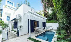 Una villa moderna con piscina, mobiliario exterior y abundante vegetación.