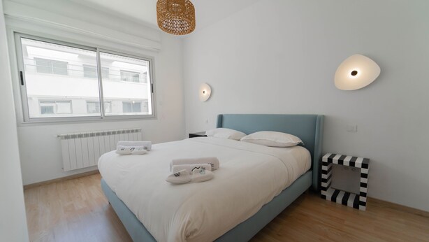 Ein Schlafzimmer mit Bett, Fenster, Heizkörper, Wandleuchte und Nachttisch.