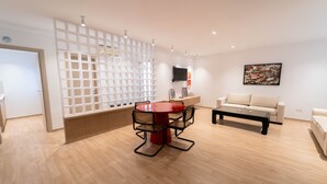 Ein modernes Wohnzimmer mit einem runden roten Tisch, zwei Sofas, einem Couchtisch und einem an der Wand montierten Fernseher.