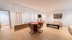 Ein modernes Wohnzimmer mit einem runden roten Tisch, zwei Sofas, einem Couchtisch und einem an der Wand montierten Fernseher.