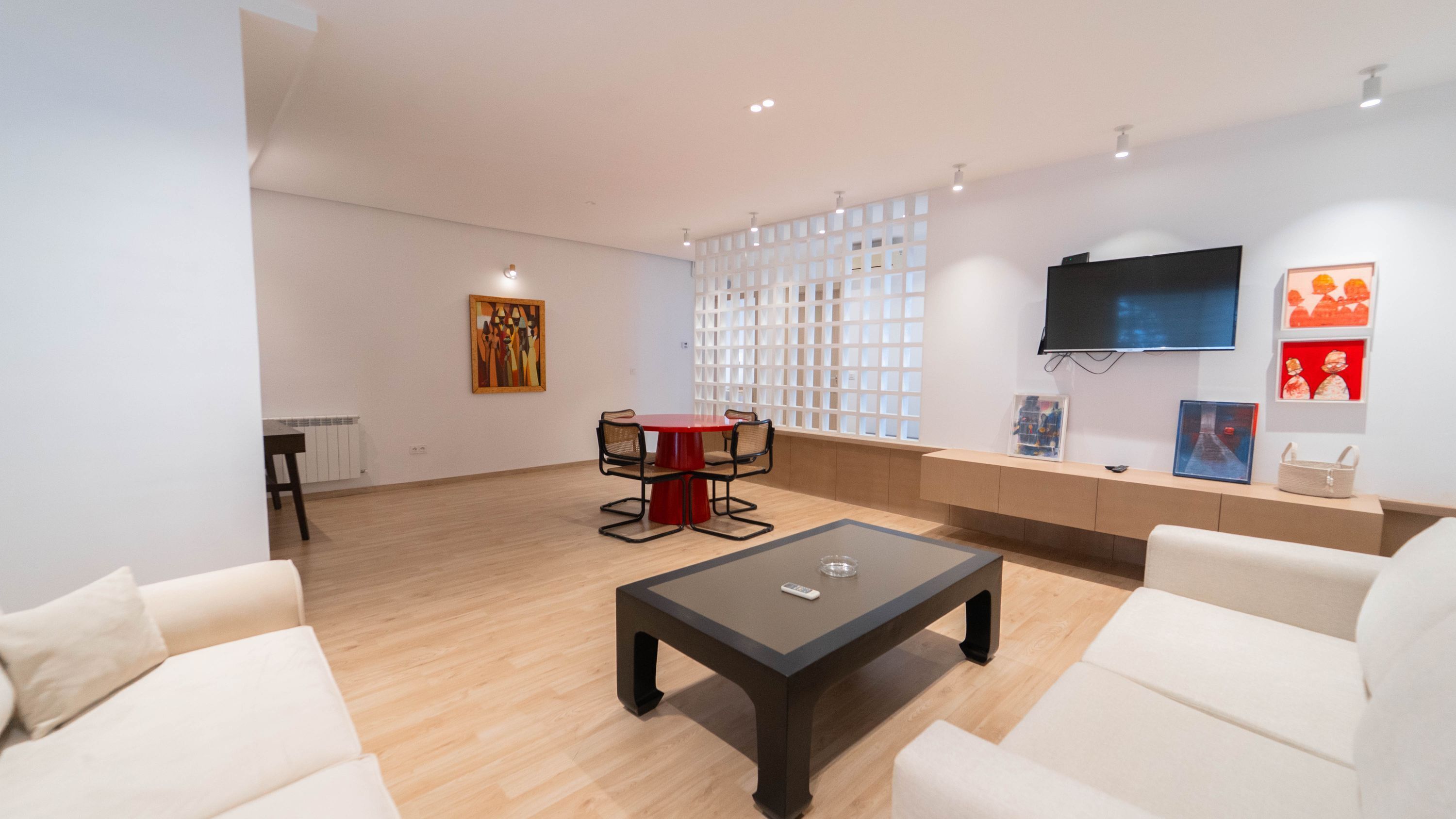 Ein modernes Wohnzimmer mit einer Couch, einem Couchtisch, einem roten Tisch mit Stühlen, einem an der Wand montierten Fernseher und Kunstwerken an den Wänden.