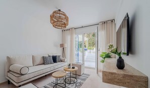 Ein modernes Wohnzimmer mit einer Couch, einem runden Couchtisch, einer Stehlampe und einem großen Fernseher, der an der Wand angebracht ist.