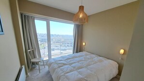 A bedroom with a large bed, a chair, a radiator, and a view of a parking lot through a window. - Sea View Family Stay for 8 (Koksijde)