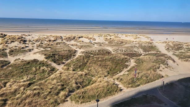 A coastal landscape with dunes, a clear sky, and a distant view of the sea. - Sea View Family Stay for 8 (Koksijde)