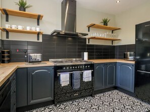 Eine moderne Küche mit Herd, Backofen und schwarzen Schränken. Darüber befinden sich Holzregale mit Tassen und Gläsern.