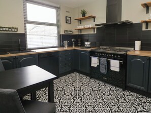 A kitchen with black cabinets, a stove, a sink, and a window with blinds. - 5 Thornbarrow Road (Windermere)