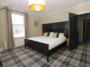 A bedroom with a bed, a headboard, a window with curtains, a radiator, and a plaid carpet. - 5 Thornbarrow Road (Windermere)