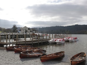 Ein Steg am Seeufer mit hölzernen Booten, ein Gebäude mit der Aufschrift 'Lakeview' und ein bewaldeter Hügel im Hintergrund.