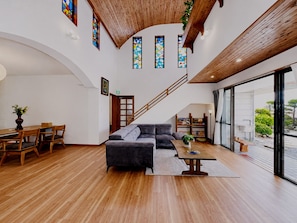 Amplia sala de estar con escalera de madera, un sofá, una mesa de comedor con sillas y ventanas grandes con vidrieras.
