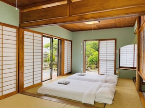 Una habitación tradicional japonesa con suelo de tatami, puertas correderas y una cama con ropa blanca.