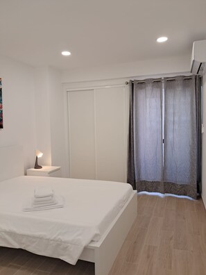 Ein Schlafzimmer mit einem Bett, einem Nachttisch mit Lampe, einem Kleiderschrank und einem Fenster mit Vorhängen.