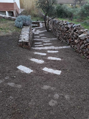 A stone pathway leading to a rustic building with a stone wall and a small wooden structure. - SA MARINA HOUSE #3. Cozy house for families with children, youth and animal (Sassari)