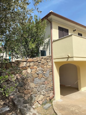 Un bâtiment avec un mur en pierre, une entrée couverte et un ciel dégagé.
