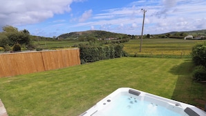 A hot tub in a backyard with a wooden fence, a grassy lawn, and a hilly landscape in the background. - Bella Vista (Llandudno)