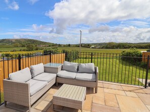 A patio with wicker furniture and a glass table, overlooking a green landscape. - Bella Vista (Llandudno)
