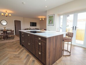 A modern kitchen with a large island, wooden cabinets, and a dining area with a table and chairs. - Bella Vista (Llandudno)