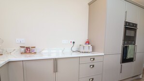 A kitchen with a white countertop, a toaster, a fire extinguisher, and a double oven. - Bella Vista (Llandudno)