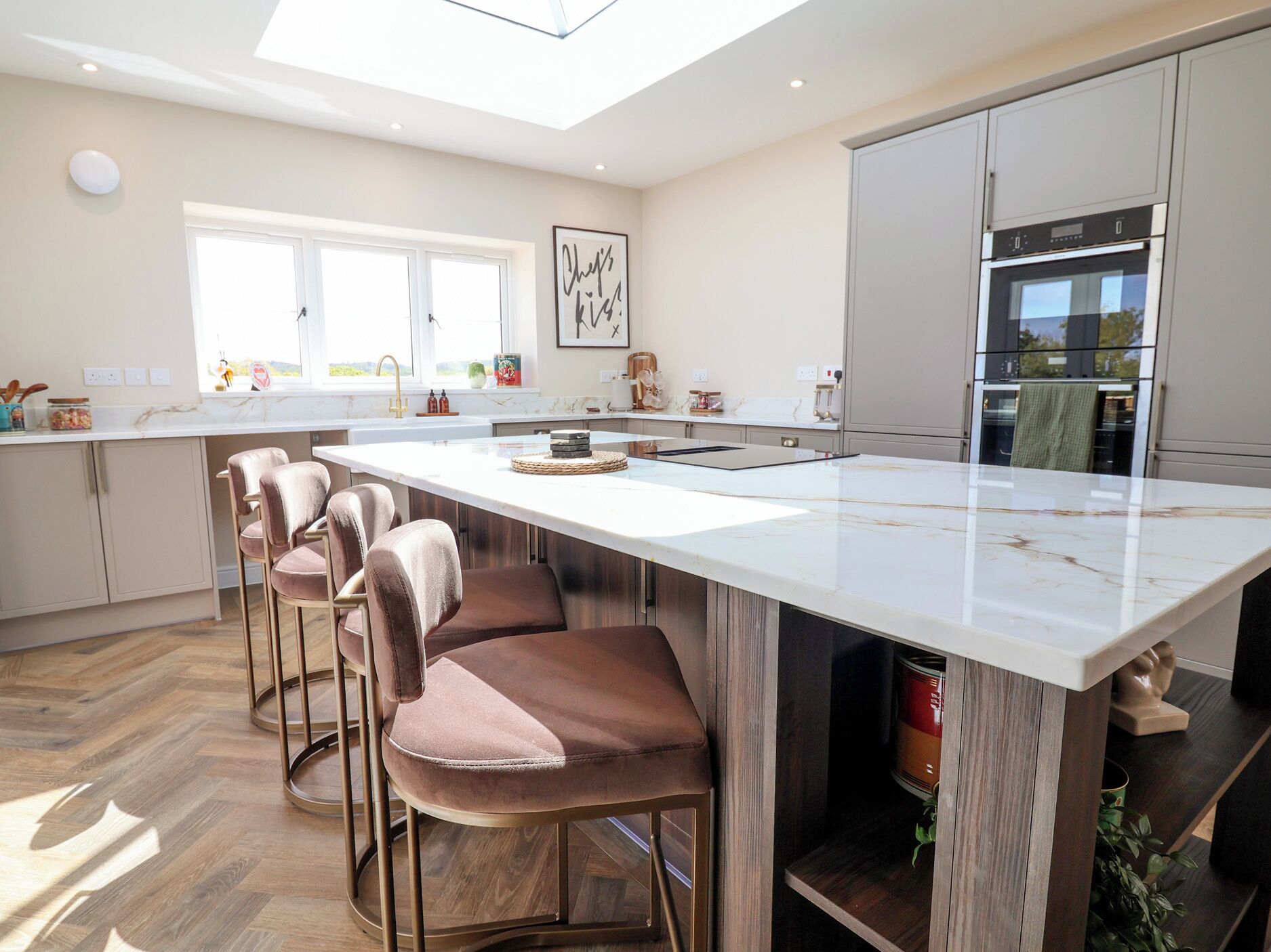 A modern kitchen with a large island, bar stools, and a built-in oven.