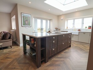 A modern kitchen with a central island, large windows, and a herringbone wood floor. - Bella Vista (Llandudno)