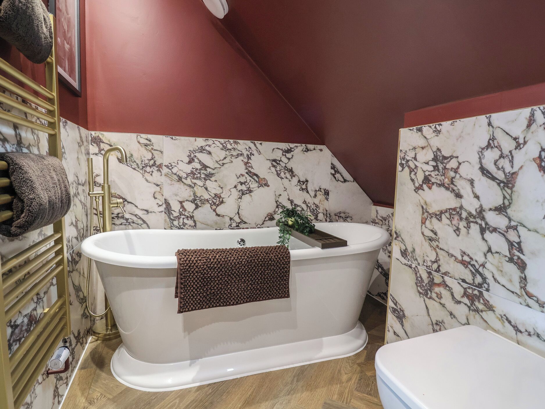 Un bagno con una vasca freestanding, pareti dal motivo marmorizzato e pavimento in legno.