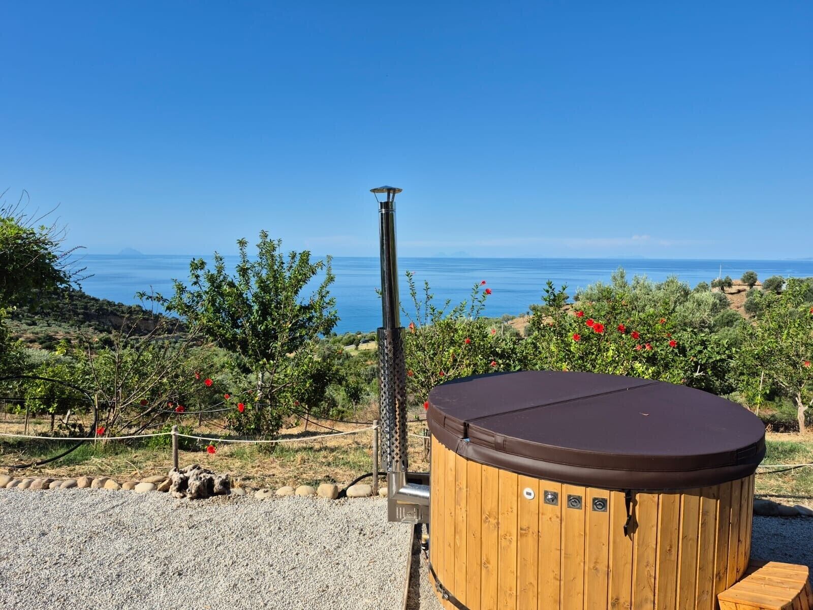 Un bain à remous avec une structure extérieure en bois et un poteau en métal, placé sur fond de ciel bleu dégagé et de paysage côtier.