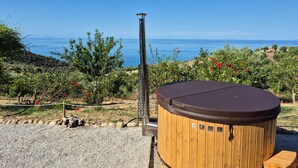 Jacuzzi con revestimiento de madera y un poste metálico, sobre un fondo de cielo azul despejado y un paisaje costero.