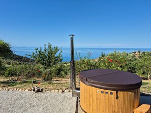 Ein Whirlpool mit Holzverkleidung und einer Metallstange, vor einer Kulisse aus blauem Himmel und einer Küstenlandschaft.