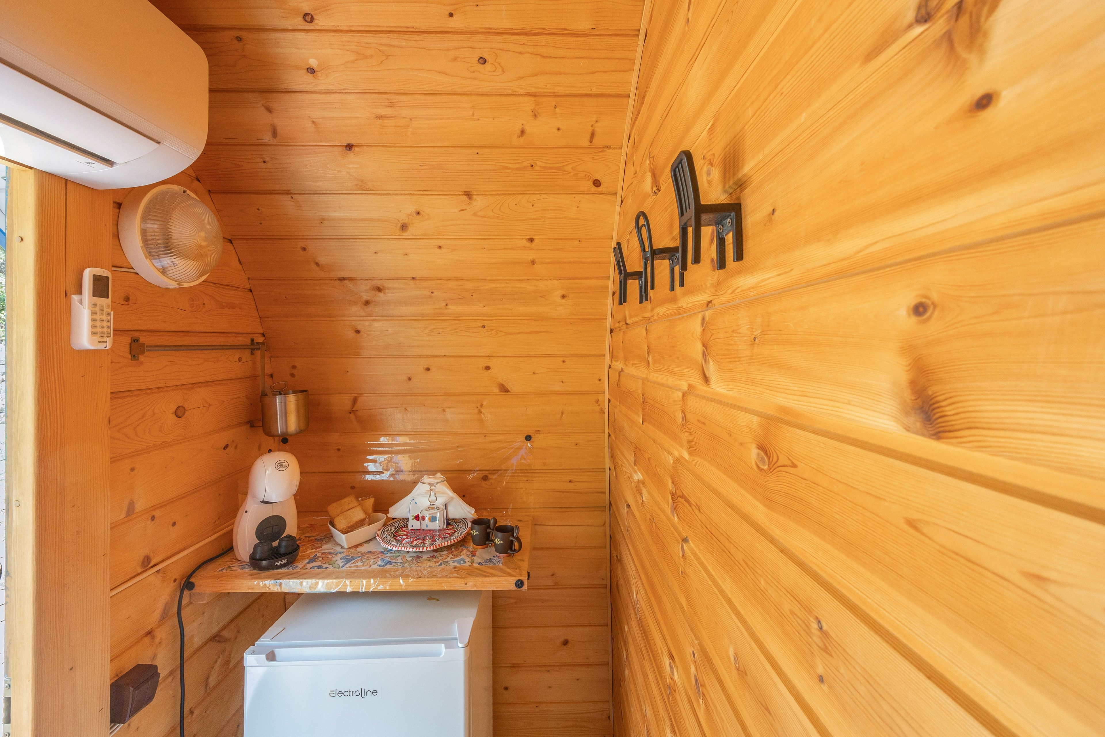 Eine gemütliche Holzhütte mit einer kleinen Küchenzeile, einem weißen Kühlschrank und einem Regal mit Wasserkocher und Tassen.