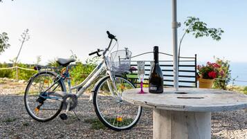 Un vélo est garé à côté d’une table sur laquelle se trouvent une bouteille et un verre, ainsi qu’une chaise, et on aperçoit la mer au loin.