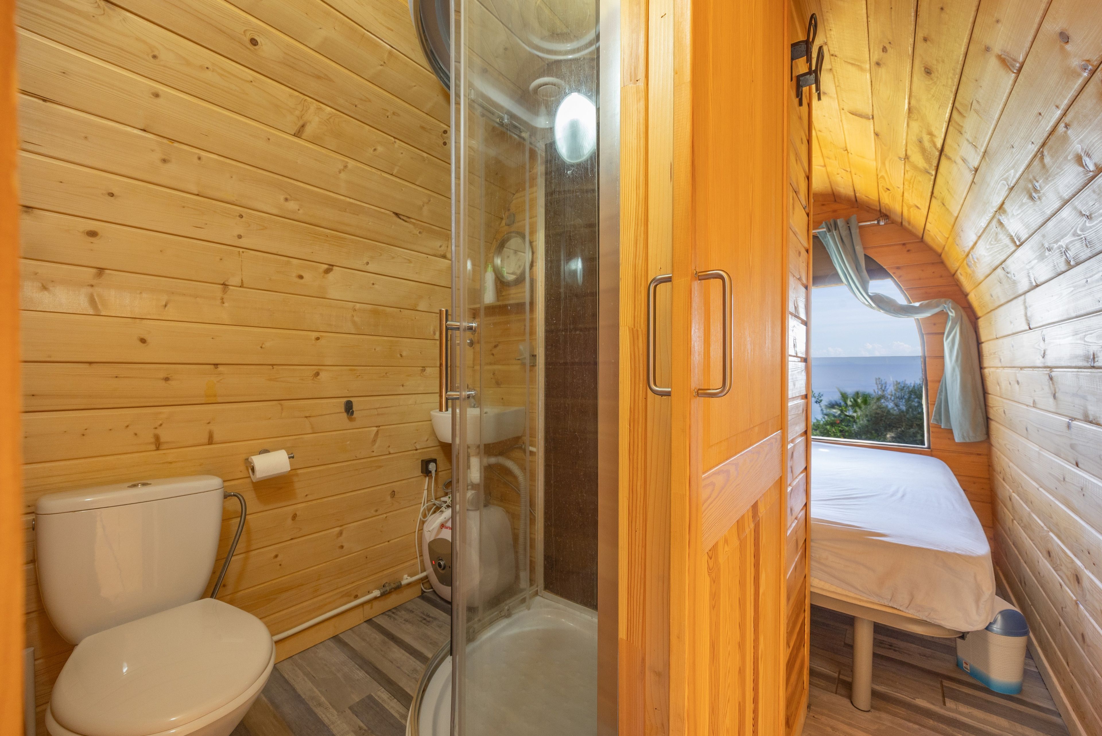 Bagno di una baita in legno con il water, doccia e un letto con vista.