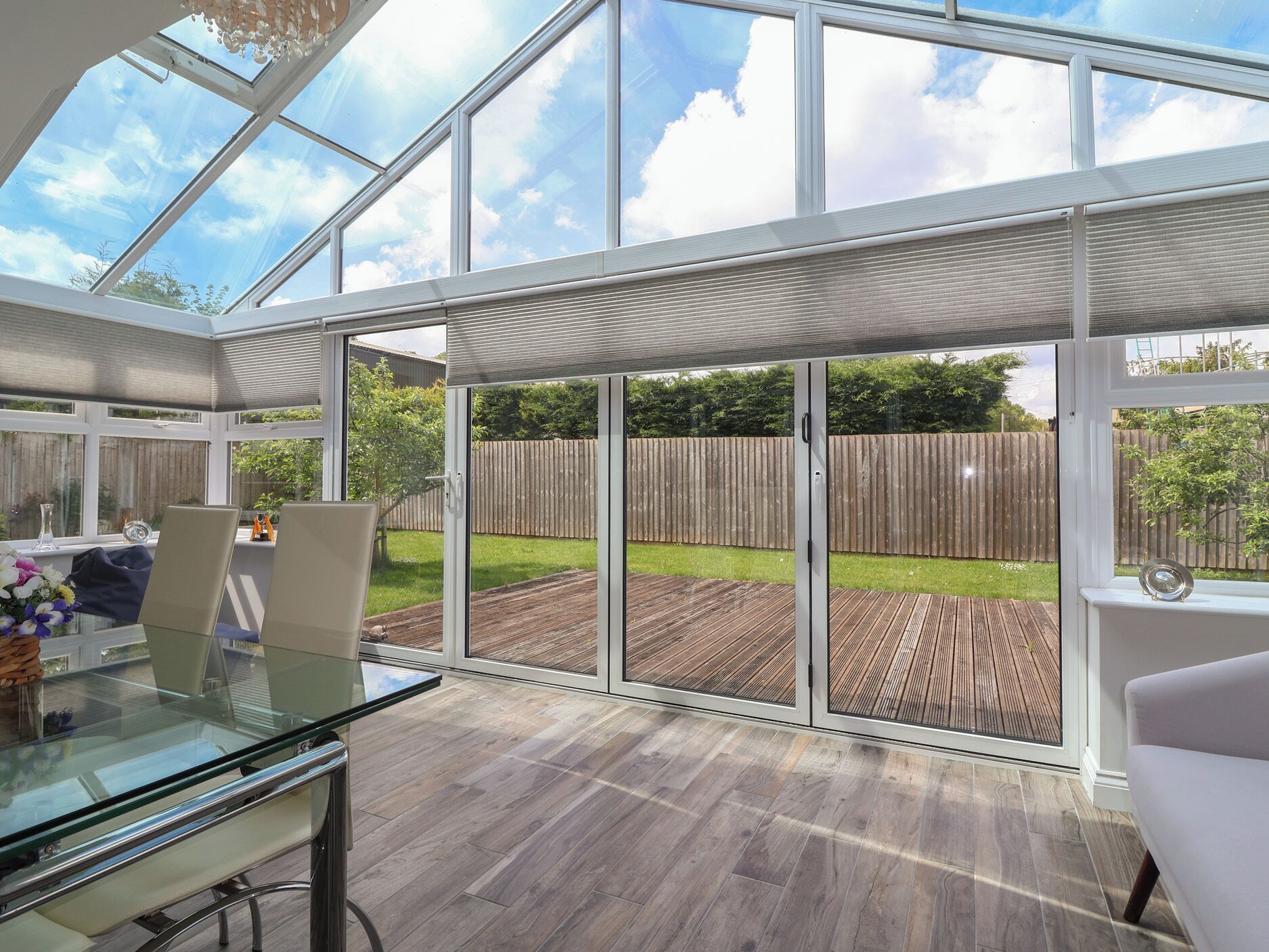 A conservatory with a glass roof, wooden deck, and a view of a backyard.