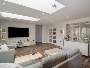 Ein modernes Wohnzimmer mit Flachbildfernseher, einer Couch, einem Couchtisch und einem Essbereich mit Glastisch.