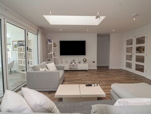Uma sala de estar moderna com televisão de tela plana, sofás brancos, uma mesa de centro e uma porta de vidro que dá para uma varanda.