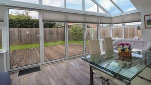 A spacious room with a glass table, chairs, and a view of a wooden deck and backyard. - Villina (Somerton)