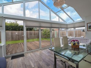 Um quarto espaçoso com mesa de vidro, cadeiras e vista para um deck de madeira e quintal.