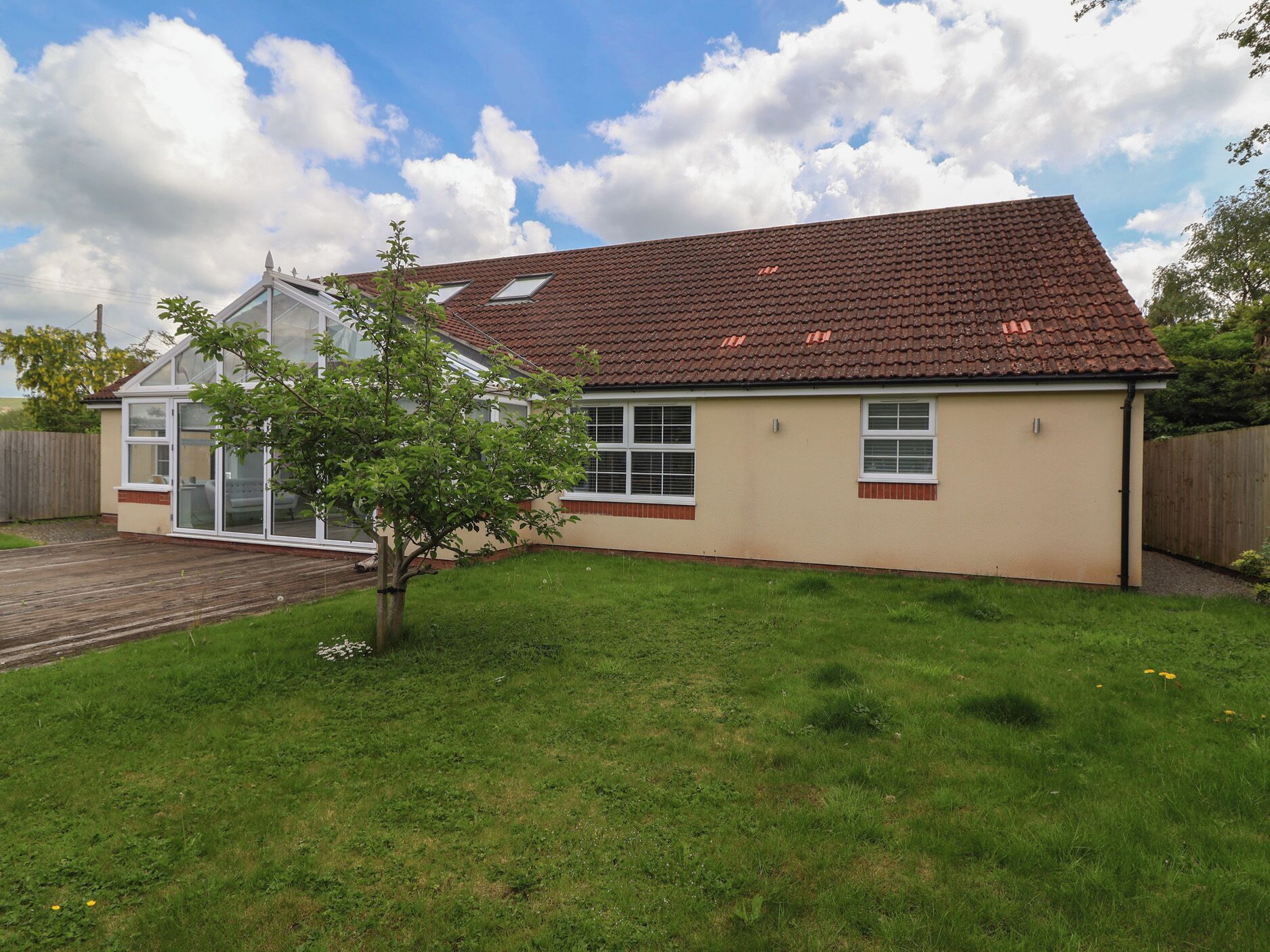 A two-story house with a tiled roof, a small garden, and a wooden deck.