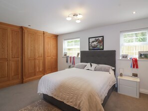 Une chambre à coucher avec un grand lit, une armoire en bois, deux tables de chevet et un luminaire au plafond.