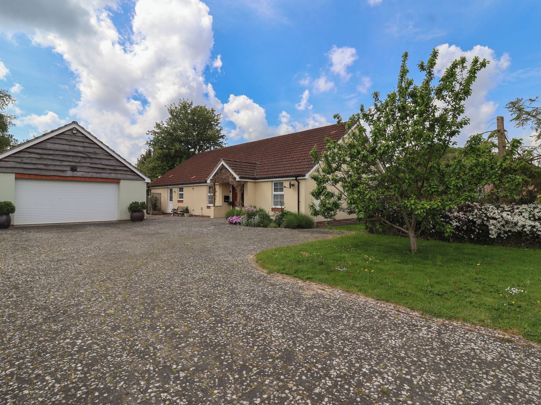 Ein Wohnhaus mit Kiesauffahrt, Garage, Veranda und Garten mit blühenden Pflanzen.