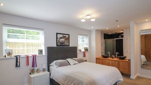 A bedroom with a large bed, a vanity with a mirror, and a window with blinds. - Villina (Somerton)