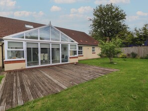 Ein Haus mit Wintergarten, Holzterrasse und umzäunter Garten.